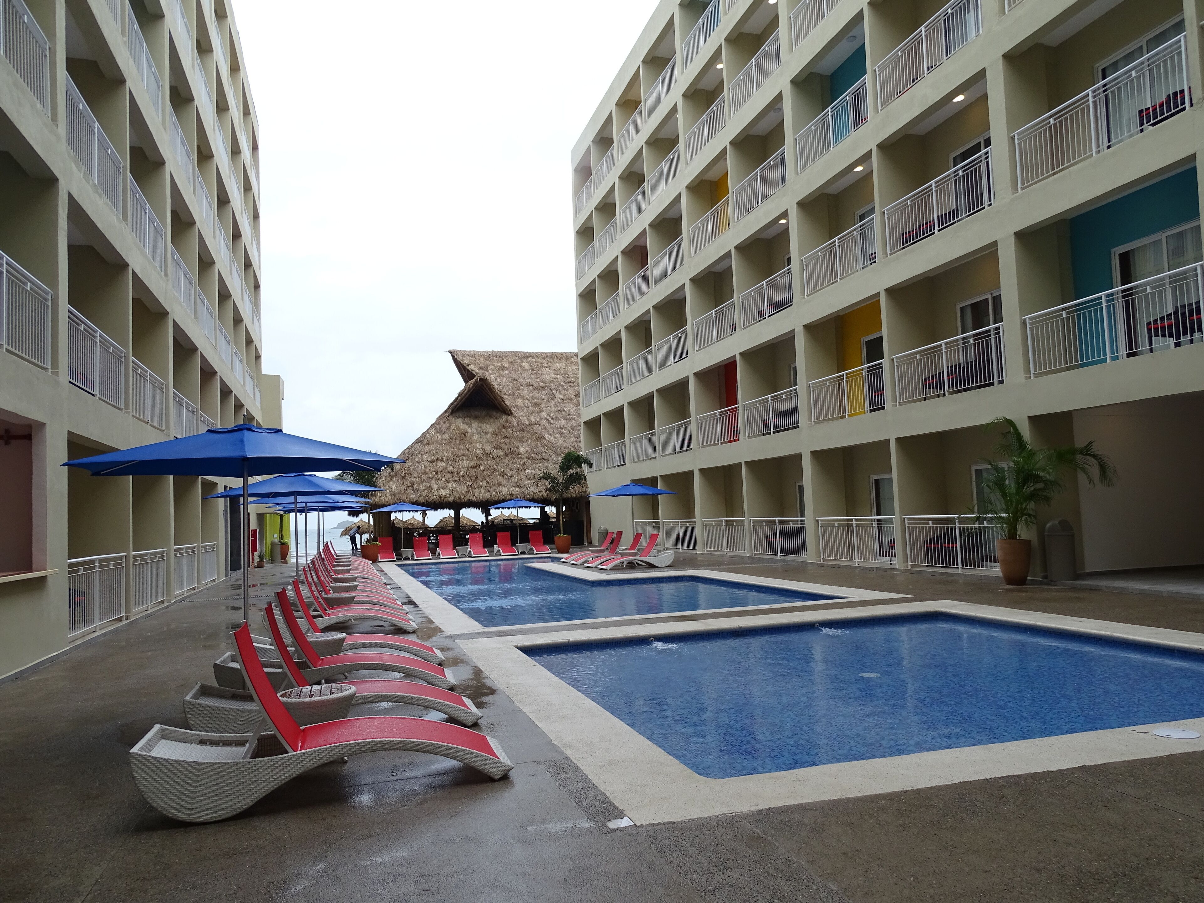 A hotel pool area with multiple swimming pools, lounge chairs, and umbrellas.