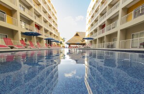 A swimming pool with tiled floors and walls, surrounded by multi-story hotel buildings with balconies and umbrellas. - Decameron Isla Coral Guayabitos Ramada All Inclusive Resort (Rincón de Guayabitos)