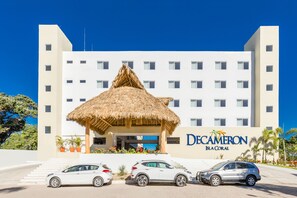 A hotel with a thatched-roof entrance, multiple floors, and a clear blue sky. - Decameron Isla Coral Guayabitos Ramada All Inclusive Resort (Rincón de Guayabitos)