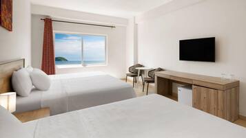 A hotel room with two beds, a desk, a TV, and a window with a view of the sea.