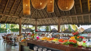A buffet area with a variety of food items, wicker hanging lights, and a thatched roof structure.