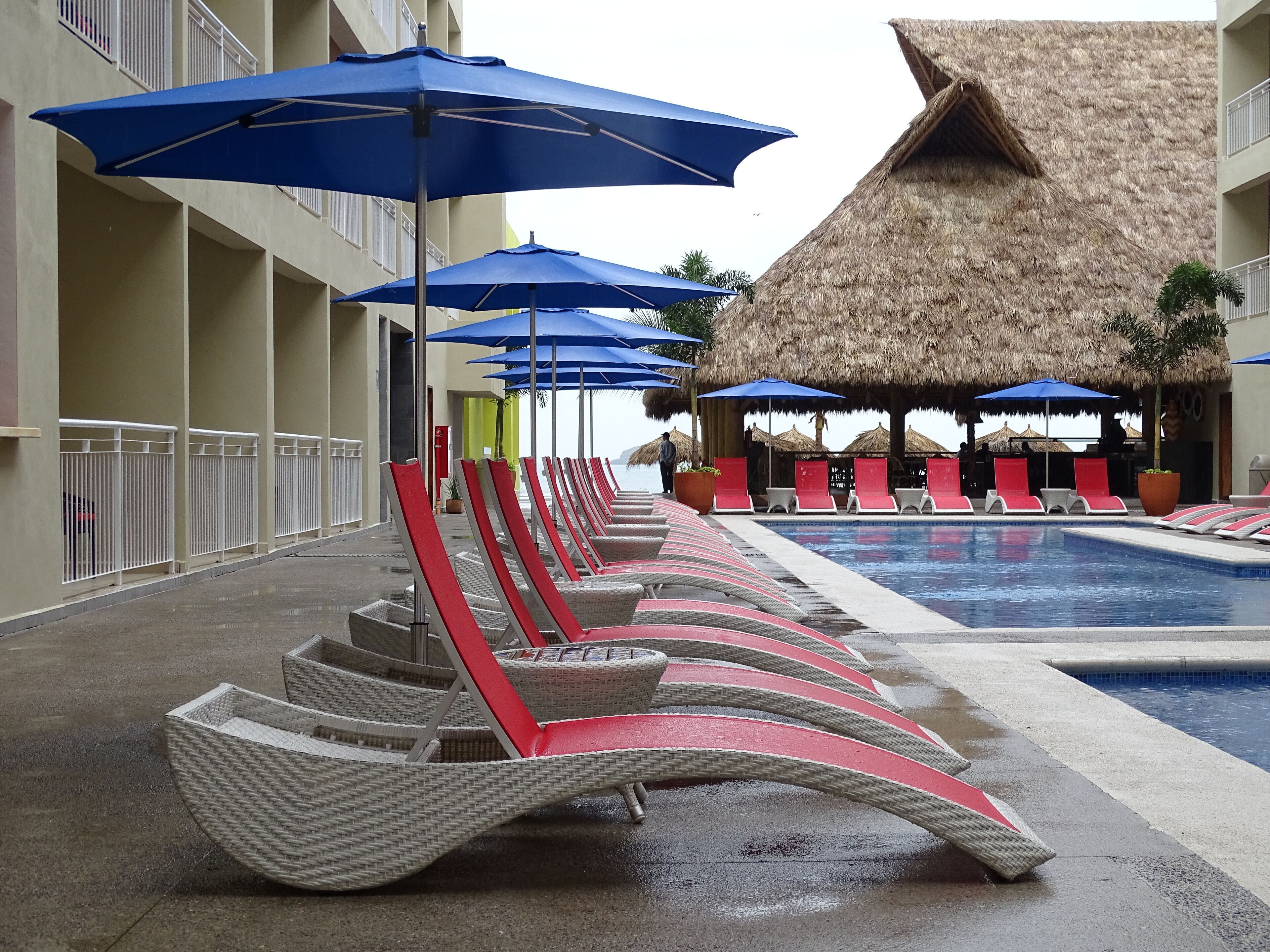 Un área junto a la piscina con sillones de descanso y sombrillas, una estructura de techo de paja y una piscina.