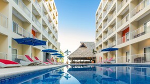 A swimming pool with lounge chairs and umbrellas, surrounded by multi-story hotel buildings with balconies.