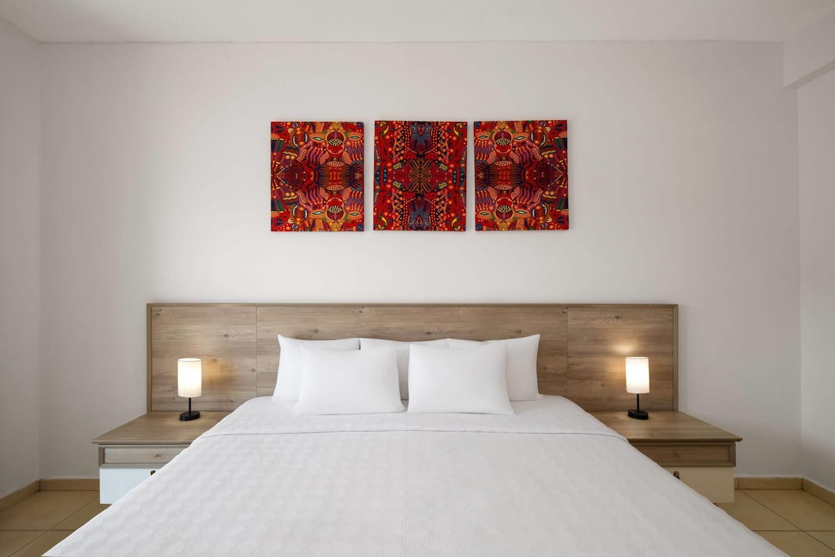 A hotel room with a large bed, two bedside tables with lamps, and three wall-mounted paintings.