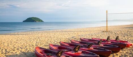 A beach with kayaks lined up and a volleyball net in the sand.