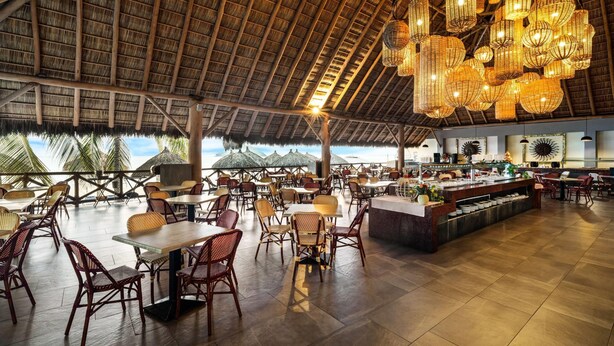 A spacious indoor dining area with high ceilings, wicker furniture, and a central bar.