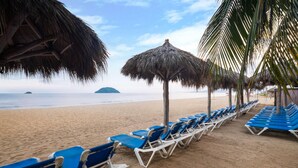 A beach with rows of blue lounge chairs and thatched umbrellas.
