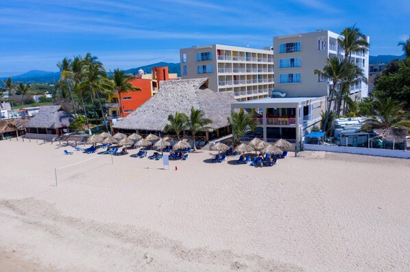 A beach with thatched-roof structures and blue lounge chairs. - Decameron Isla Coral Guayabitos Ramada All Inclusive Resort (Rincón de Guayabitos)