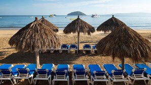 Una playa con sombrillas de paja y sillas de descanso azules.