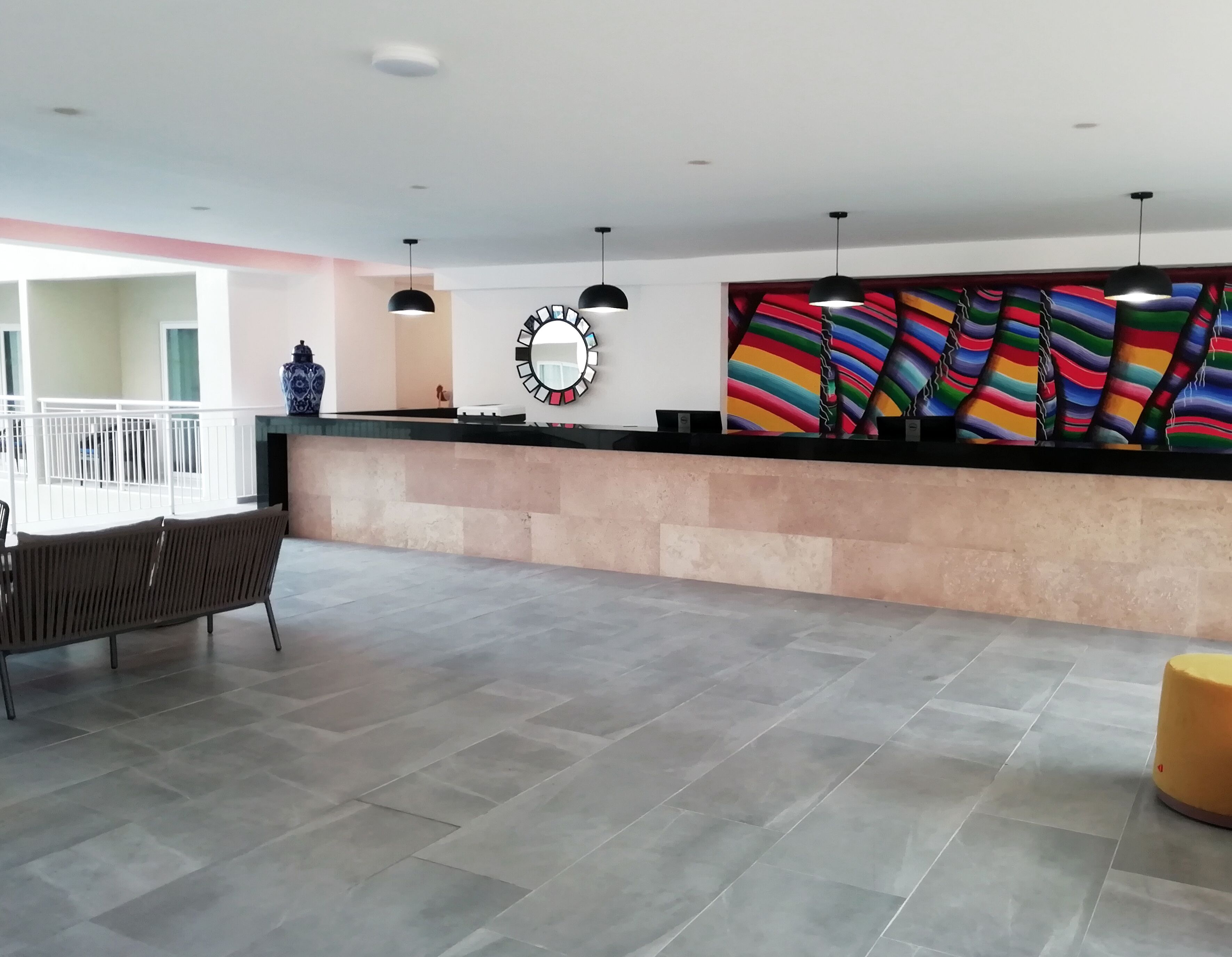 A spacious lobby with a reception desk, modern pendant lights, a colorful abstract painting, and a large mirror.
