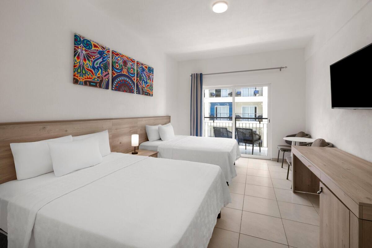 A hotel room with two beds, a desk, a TV, and a balcony with a view.