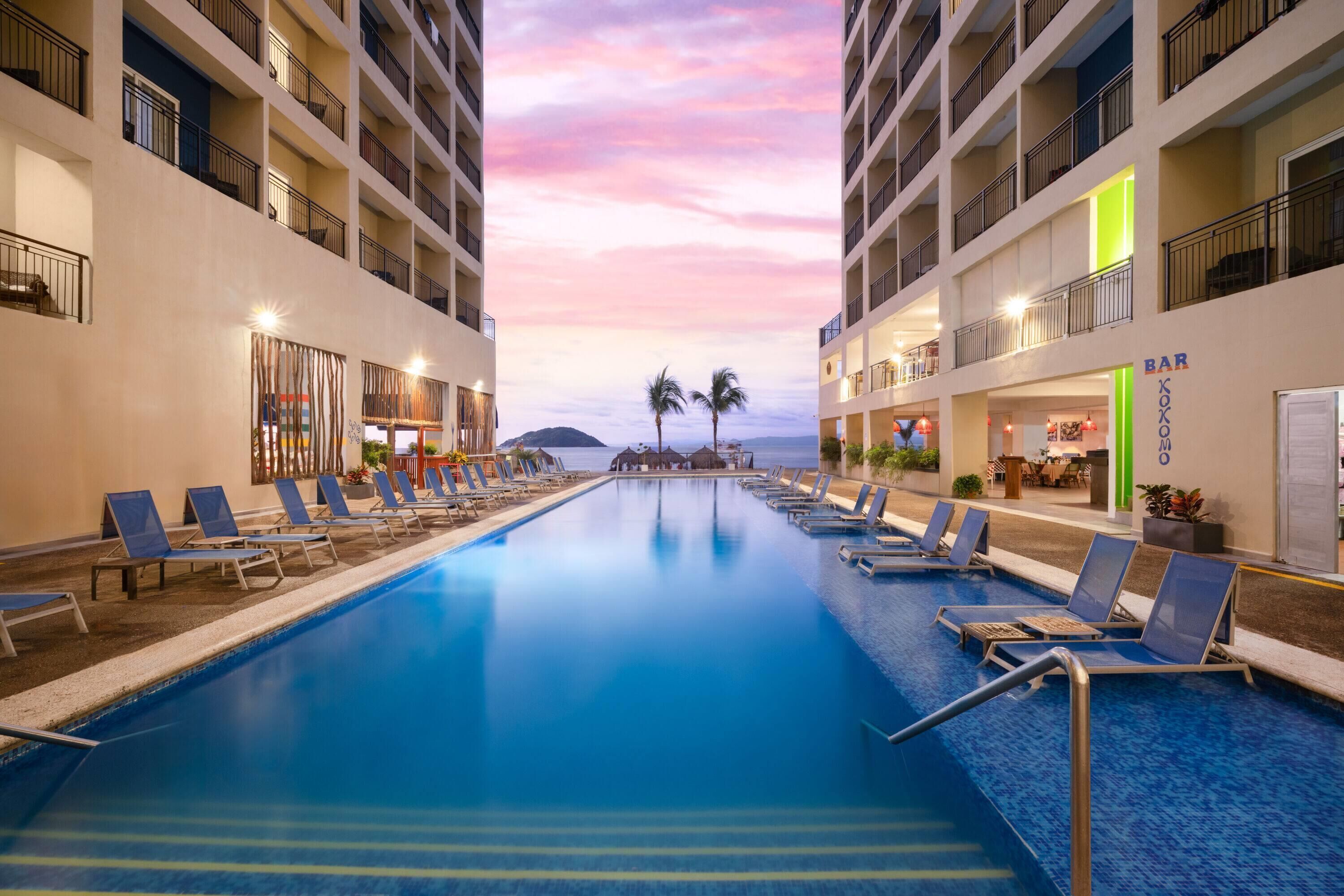 Una piscina dell'hotel con lettini, un bar e vista sull'oceano al tramonto.