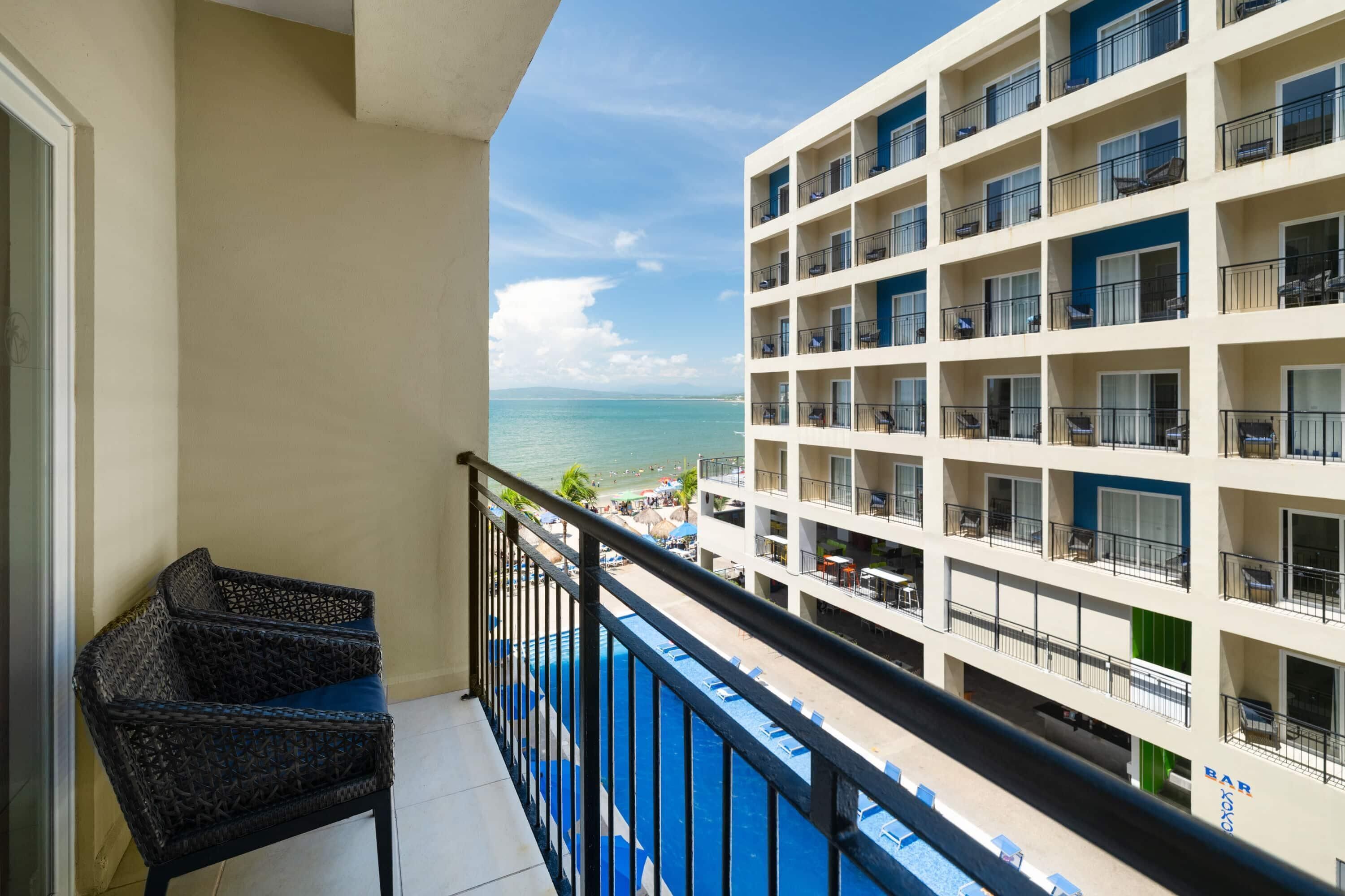 A balcony with a view of the sea, a pool, and a building with multiple balconies.