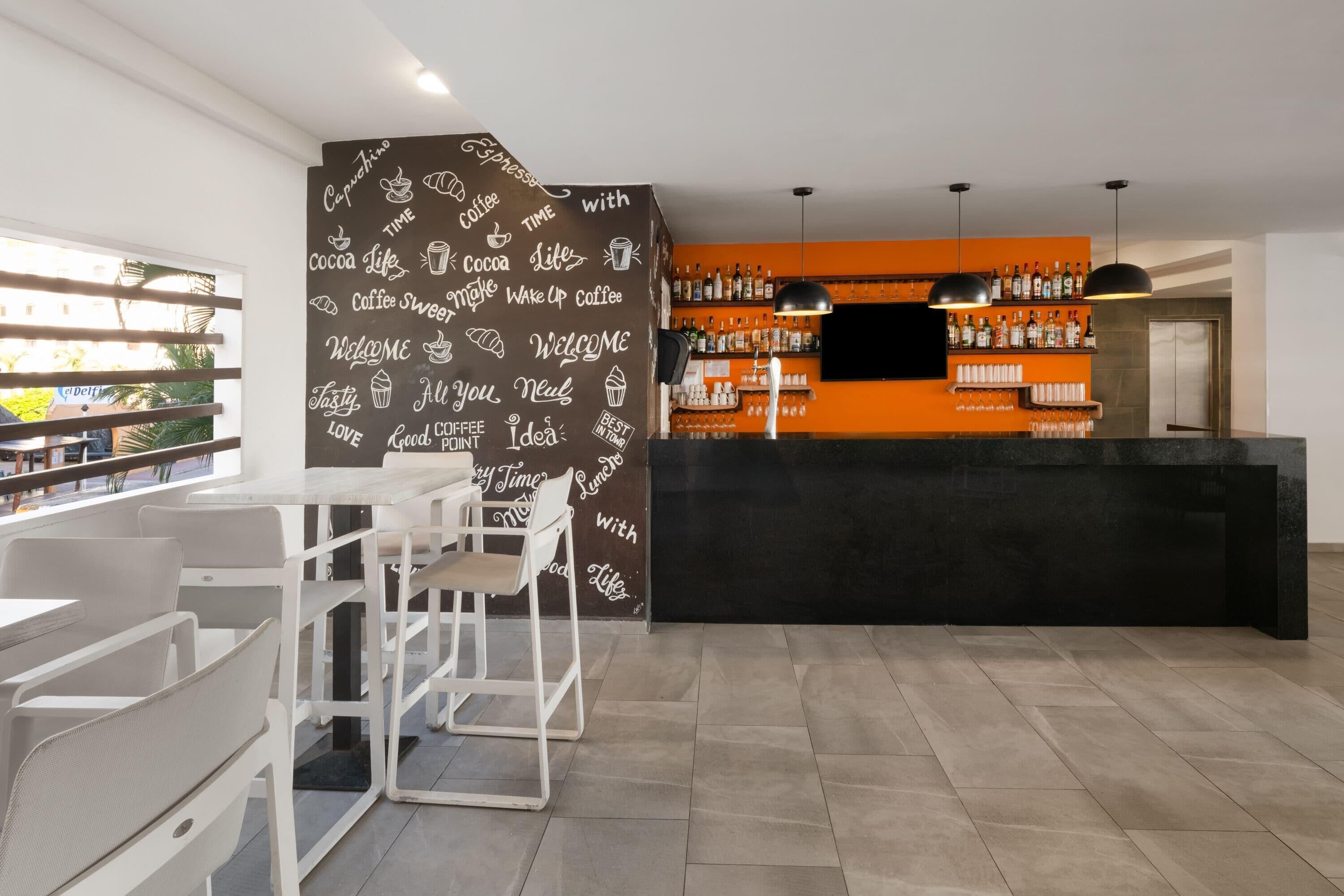 Ein moderner Barbereich mit einer schwarzen Theke, weißen Stühlen und einer Wand mit Wörtern rund um Kaffee.