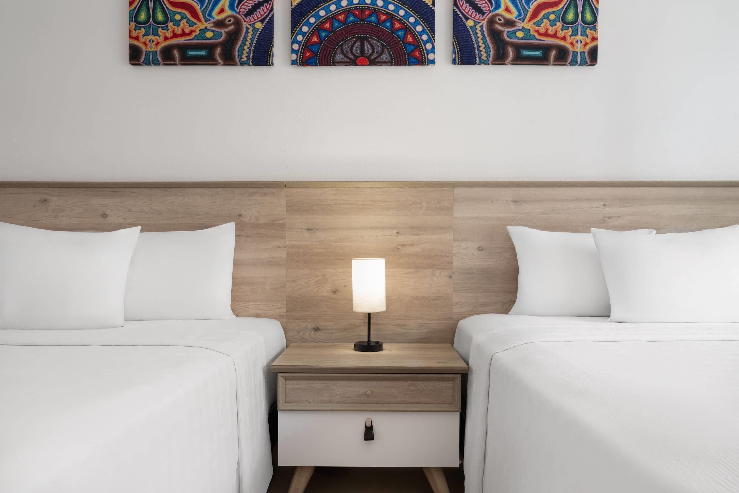 A hotel room with two single beds, a nightstand with a lamp, and a wooden headboard.