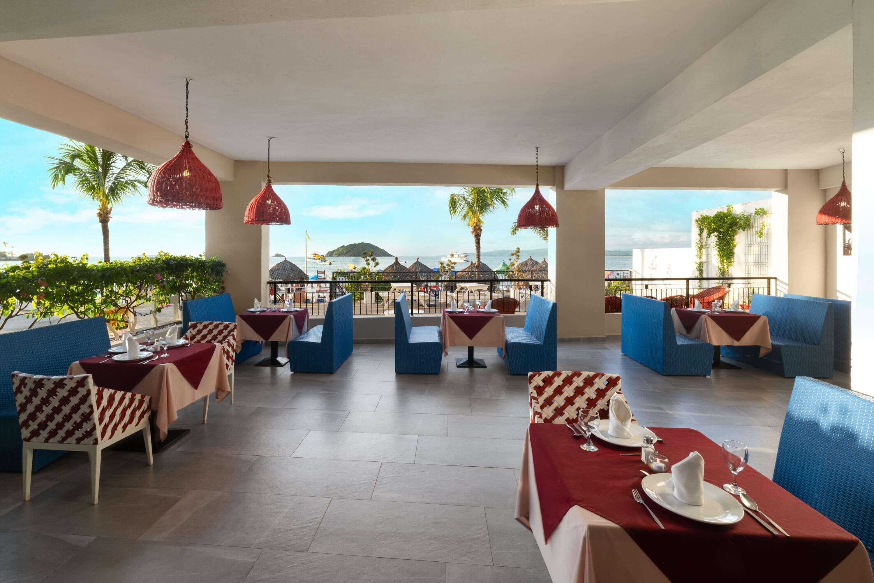 A restaurant with outdoor seating, red hanging lights, and a view of the sea.