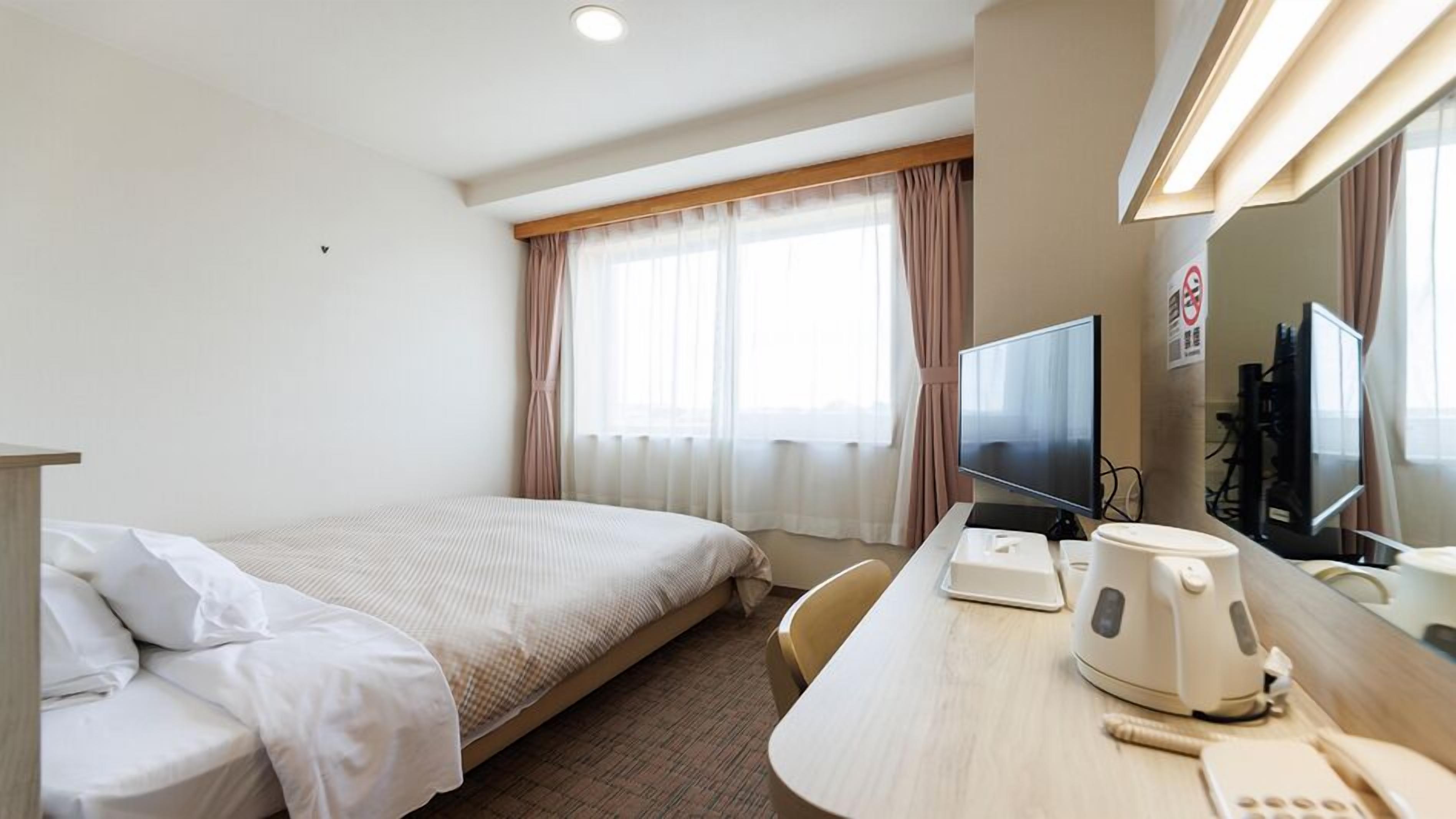 A hotel room with a bed, a desk with a computer, a coffee maker, and a TV.