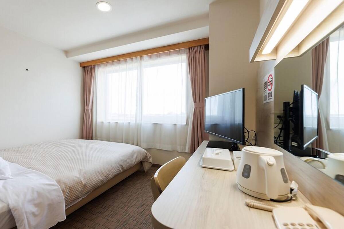 A hotel room with a bed, a desk with a computer, a coffee maker, and a TV.