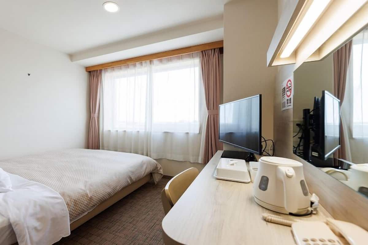 A hotel room with a bed, a desk with a computer, a coffee maker, and a TV.