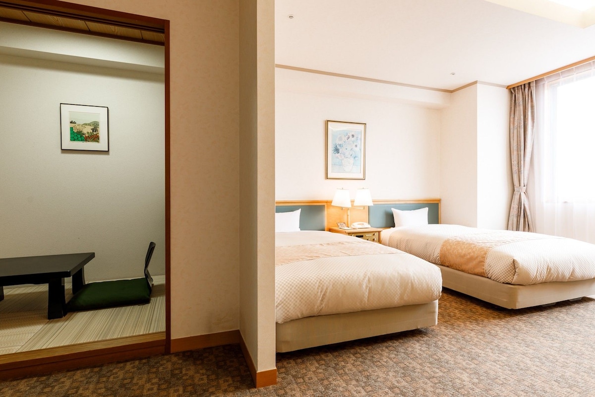 Habitación de hotel con dos camas, un escritorio, una silla, un espejo y un cuadro en la pared.