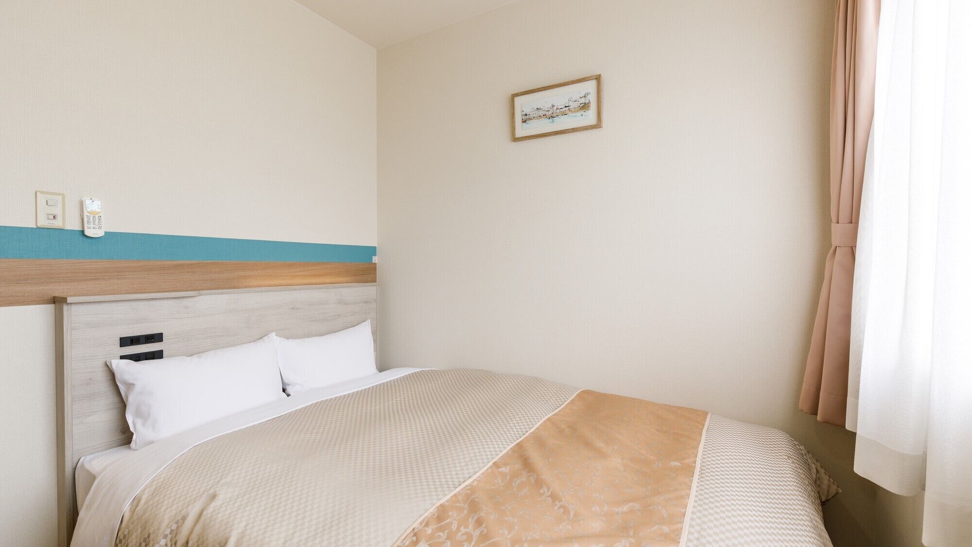 A hotel room with a bed, a headboard, a wall-mounted phone, and a framed picture.