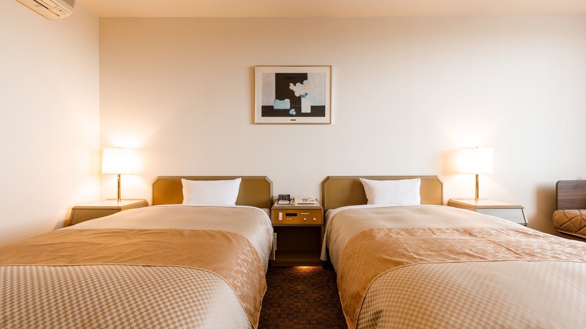 Habitación de hotel con dos camas, lámparas de noche, una mesita de noche con un teléfono y un cuadro en la pared.