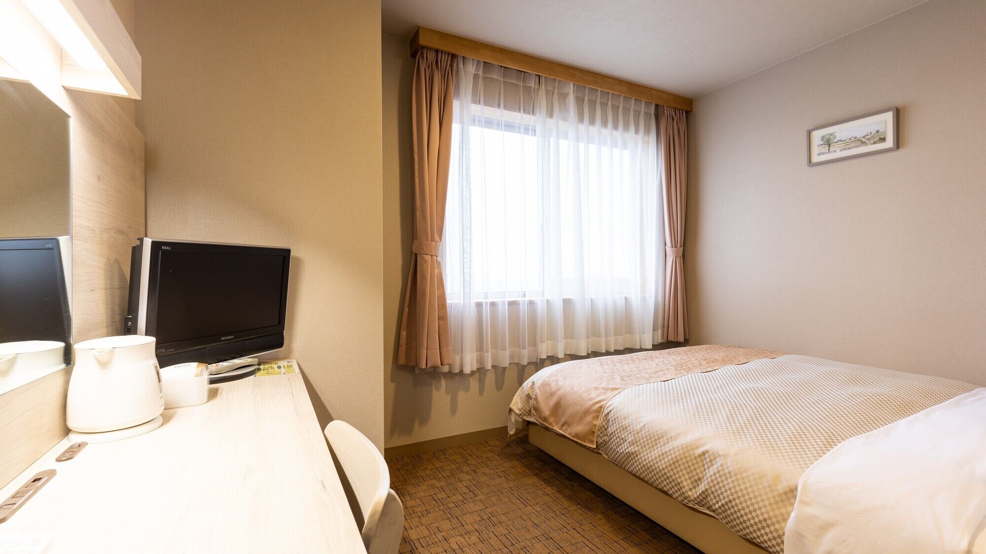 Habitación de hotel con cama, escritorio, televisor, cafetera y ventana con cortinas translúcidas.