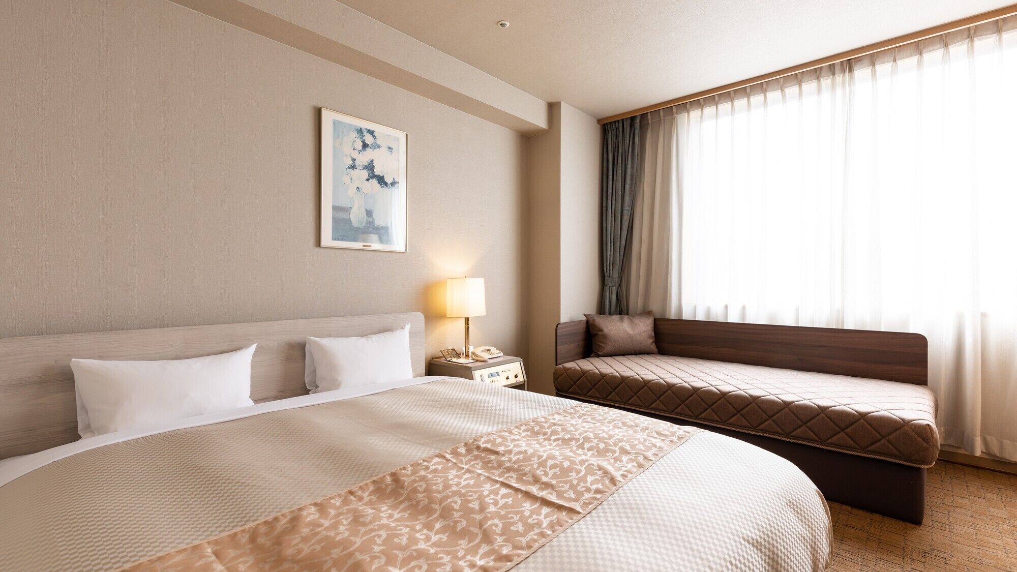 Una habitación de hotel con una cama grande, una cama más pequeña, una mesita de noche con lámpara y una ventana con cortinas.