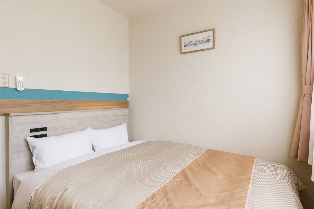 A hotel room with a bed, a headboard, a wall-mounted phone, and a picture.