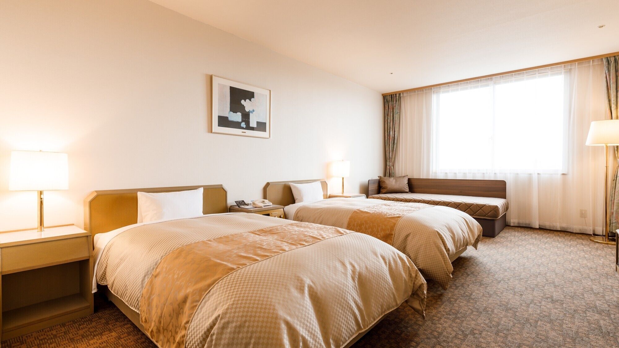 A hotel room with two beds, a large window with curtains, a framed picture on the wall, and bedside lamps.