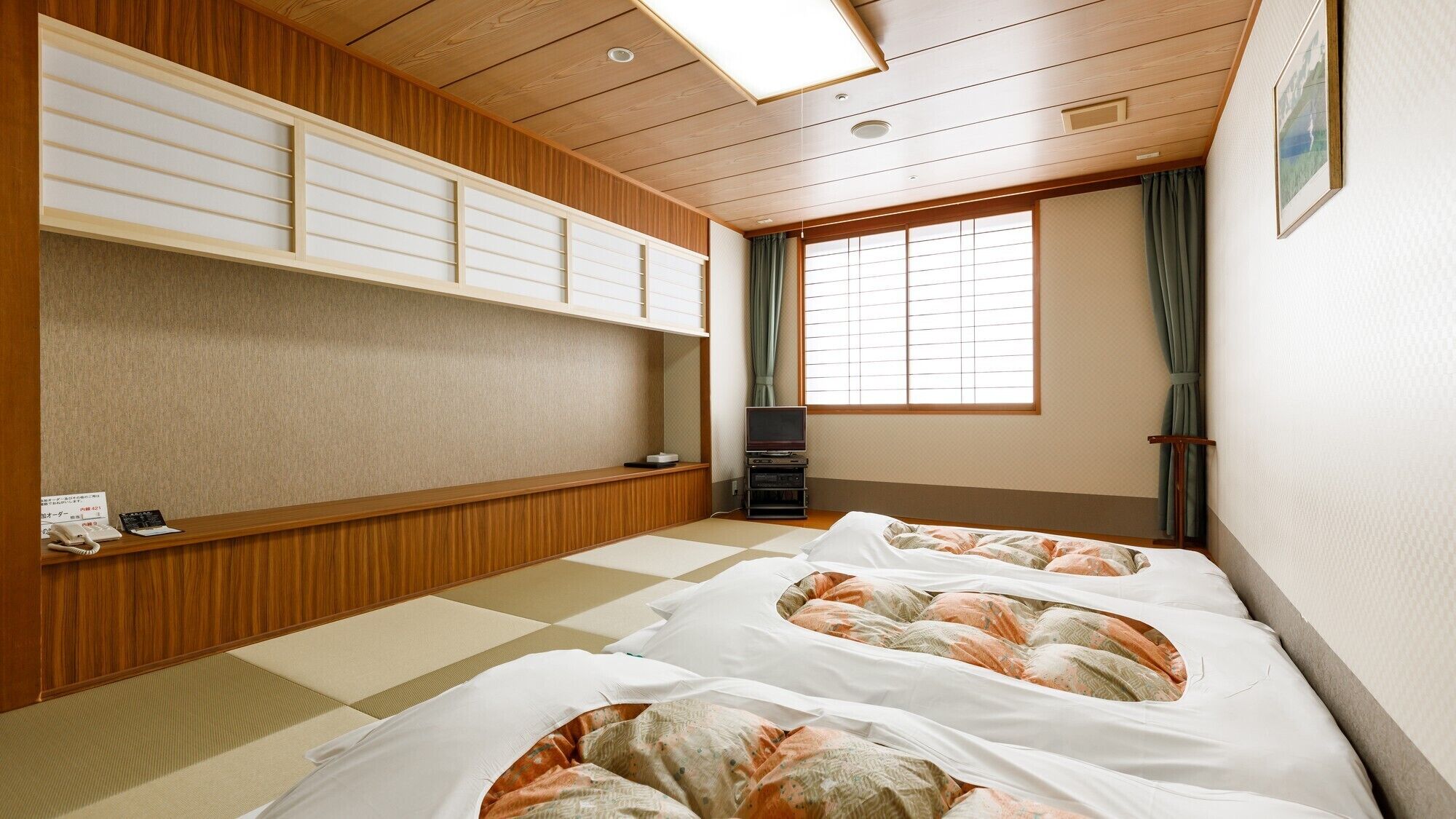 A traditional Japanese-style room with tatami flooring, a low wooden desk, a television, and a large window with curtains.