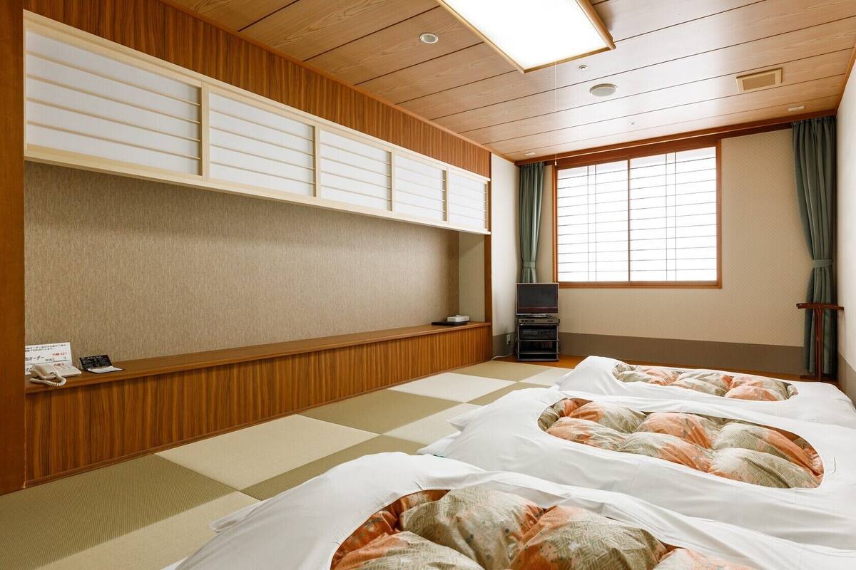 A traditional Japanese-style room with tatami flooring, a low wooden desk, a television, and a large window with curtains.
