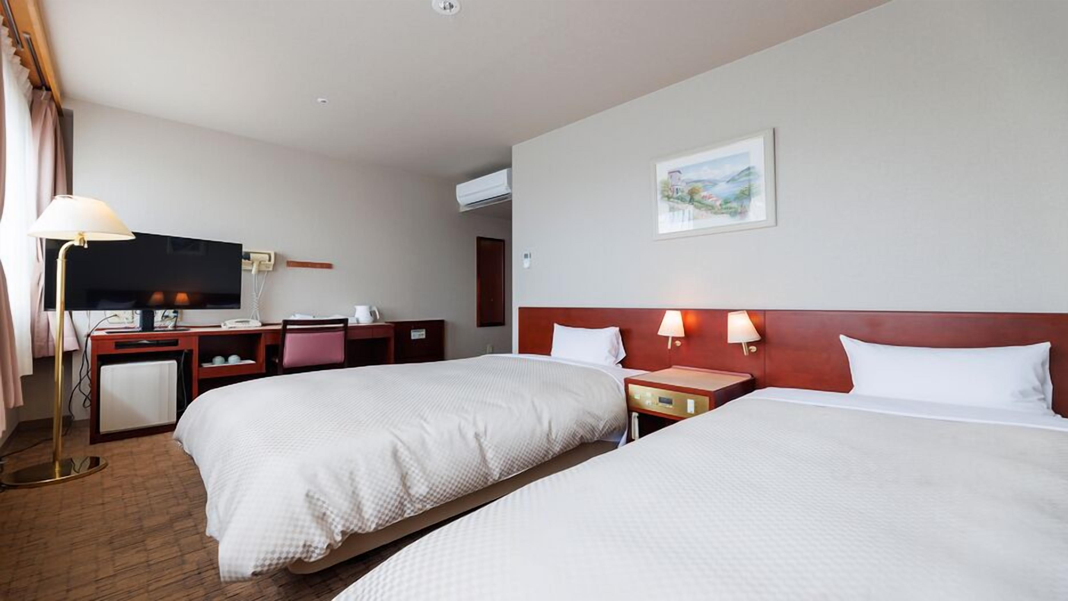 A hotel room with two beds, a desk, a television, and a painting on the wall.