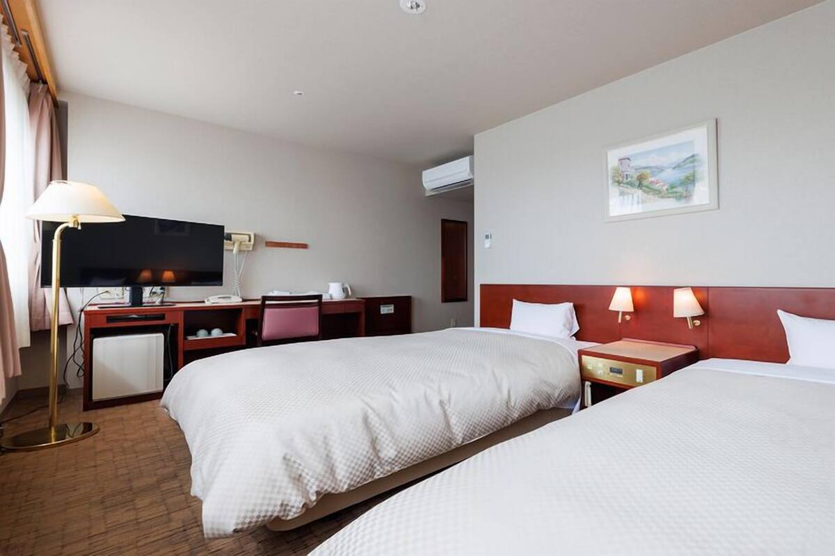 A hotel room with two beds, a desk, a television, and a painting on the wall.