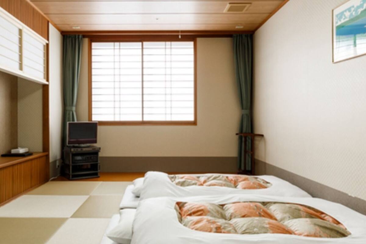 A room with two beds, a television, and a window with curtains.