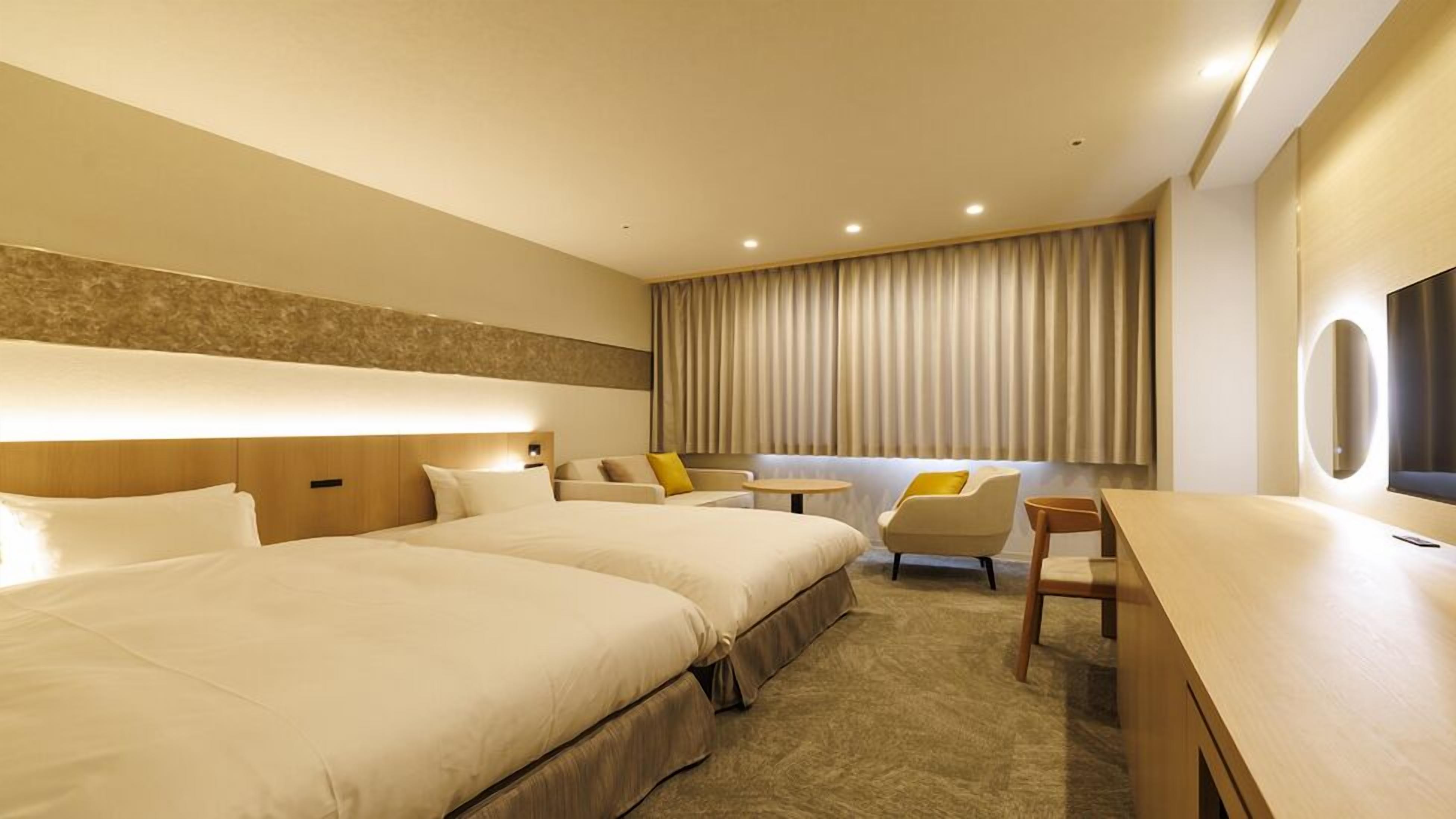 A hotel room with two beds, a sofa, a small table, and a TV.