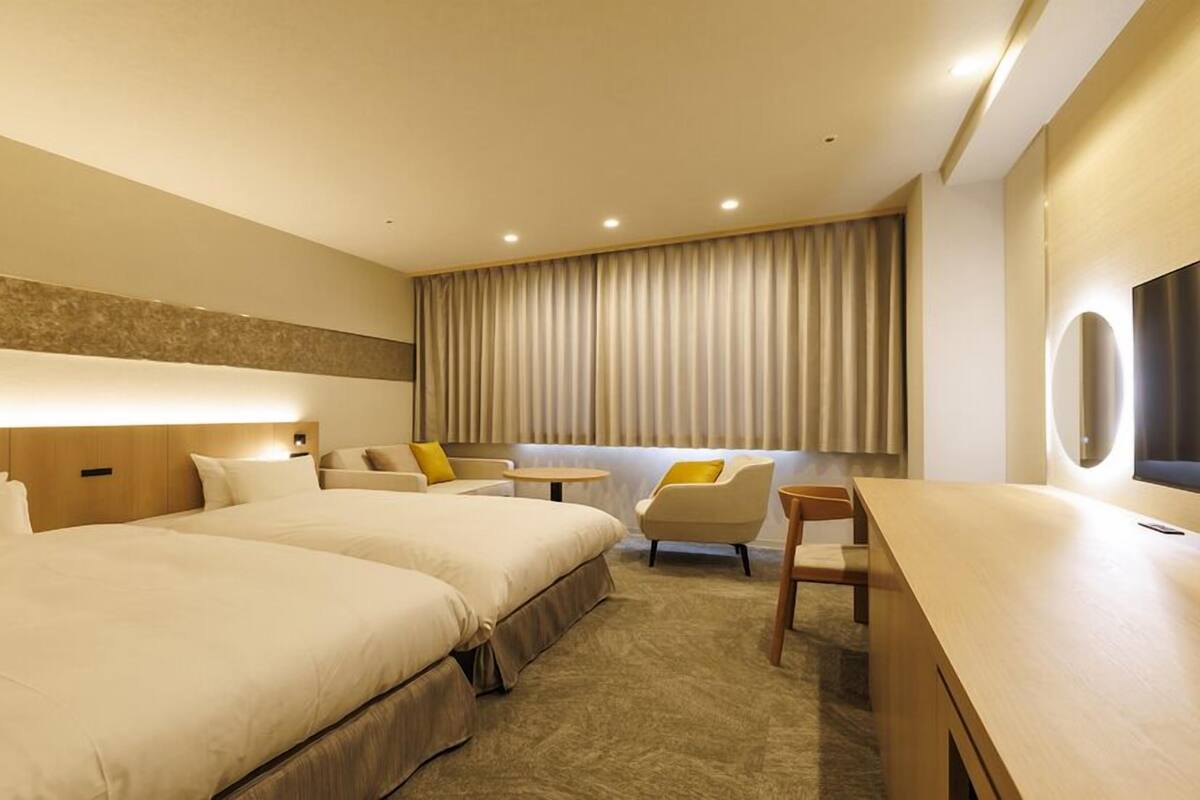 A hotel room with two beds, a sofa, a small table, and a TV.