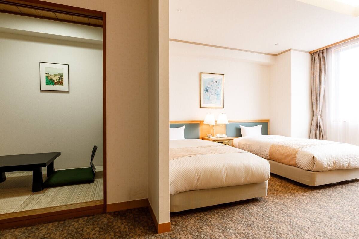 A hotel room with two beds, a desk, a chair, a mirror, and a picture on the wall.