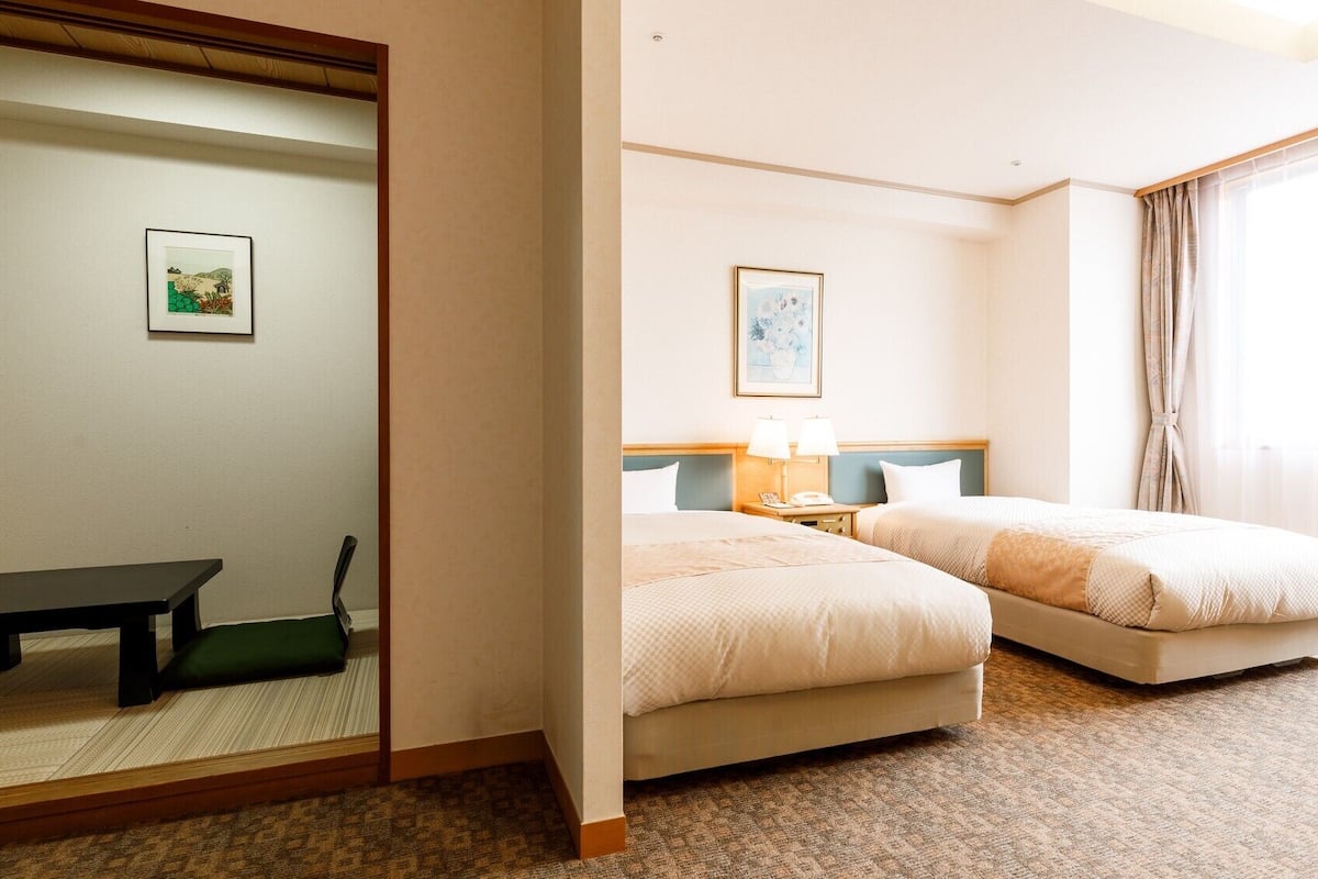 Habitación de hotel con dos camas, un escritorio, una silla, un espejo y un cuadro en la pared.