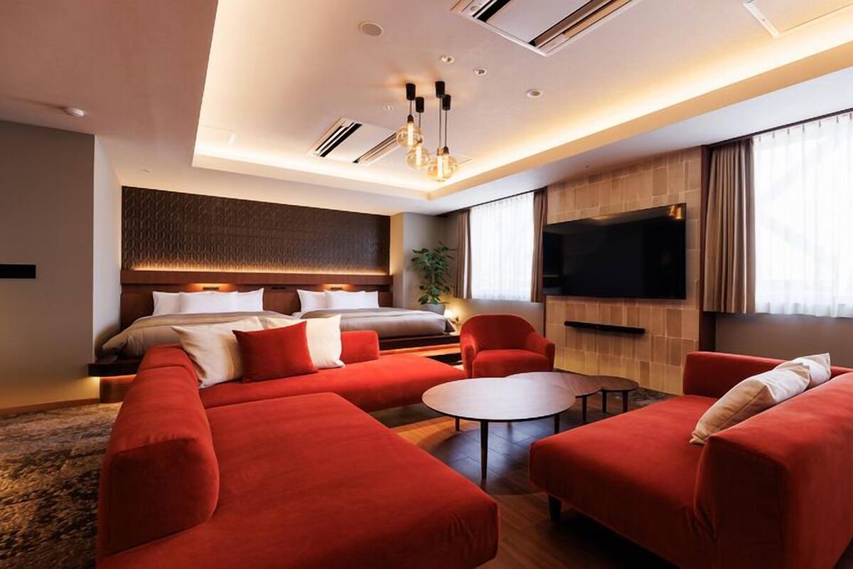 A modern hotel room with a large bed, a sofa, a coffee table, and a TV.