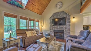 A living room with a stone fireplace, wooden ceiling, and large windows. - Updated Cabin on White River by Boat Landing! (Calico Rock)