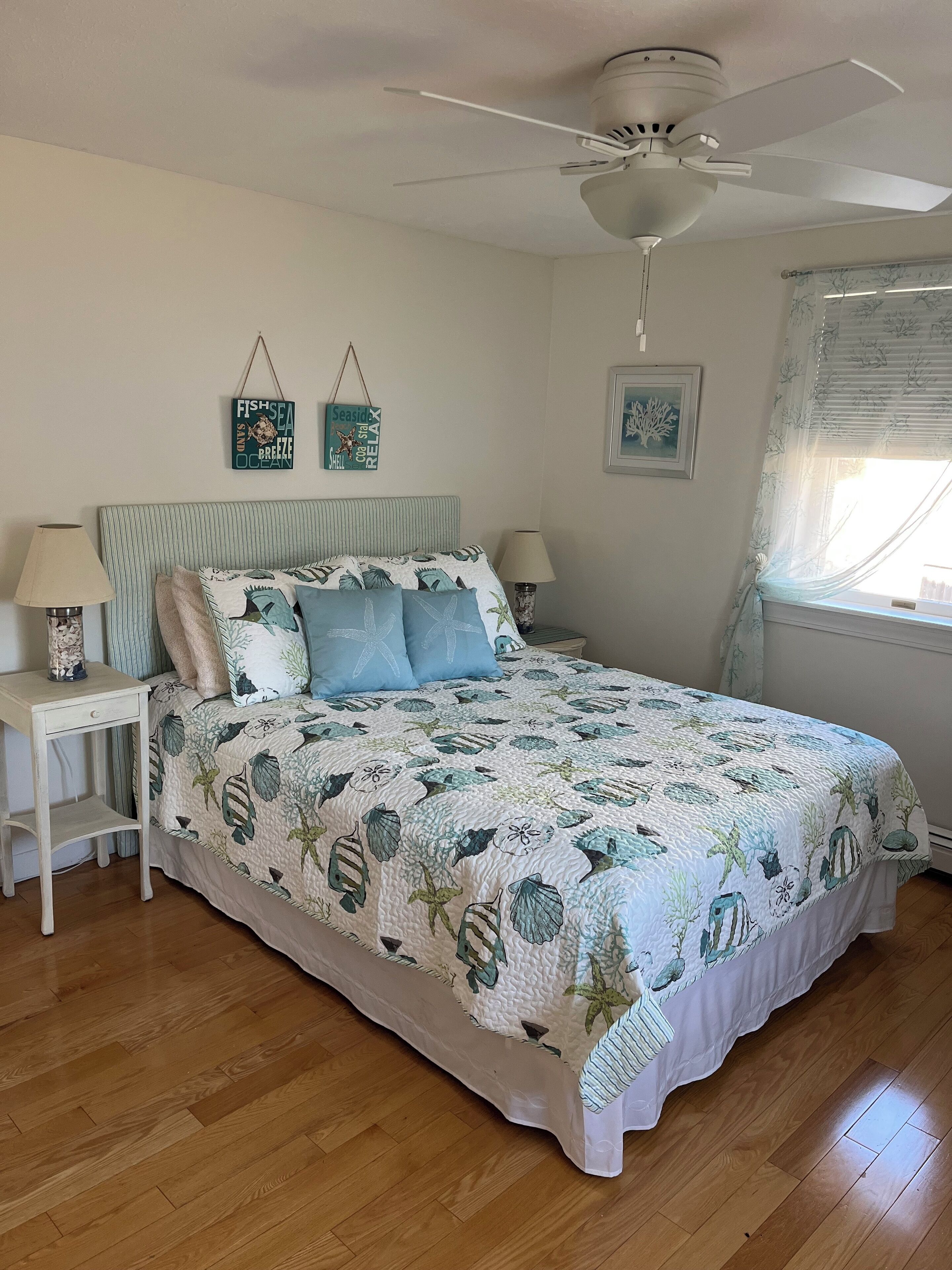 A bedroom with a bed, two bedside tables, a ceiling fan, and a window with curtains.