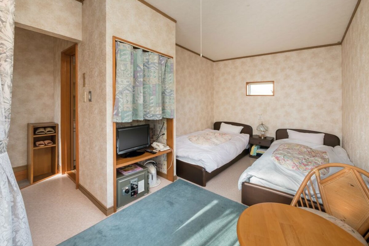 A compact hotel room with a bed, a desk with a computer, a chair, and a small table.