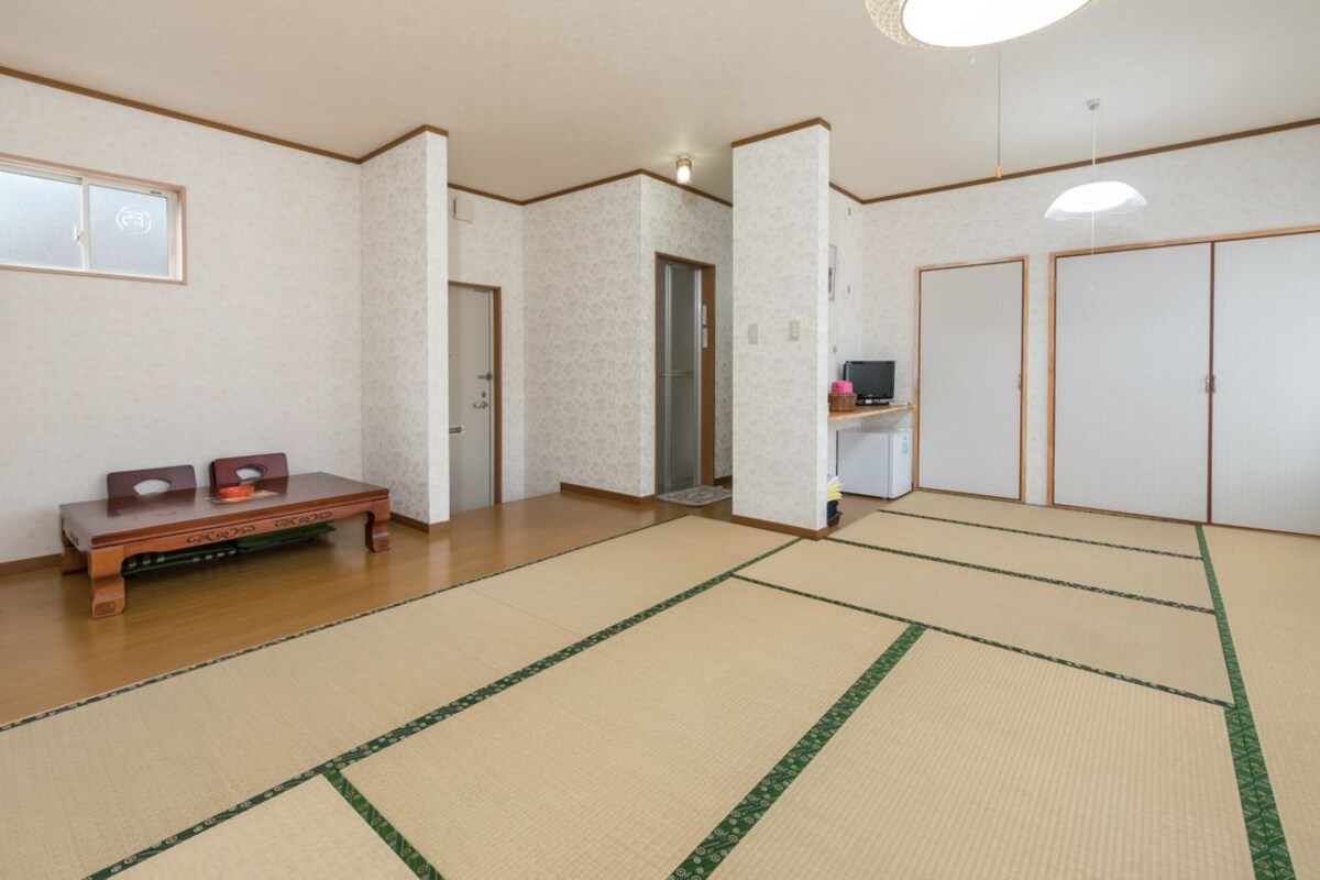 Ein traditioneller Raum mit Tatami-Matten, einer Holzbänklä, einem Schreibtisch und einer hängenden Leuchte.