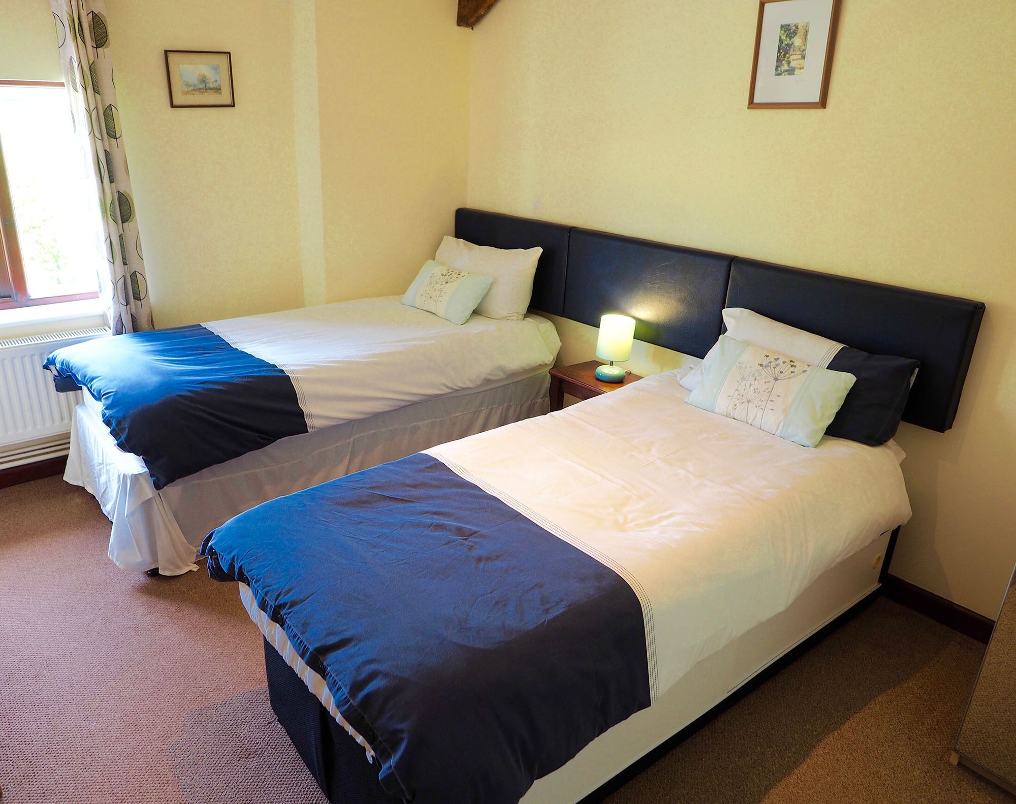 Une chambre d’hôtel avec deux lits simples, une table de chevet avec une lampe et une fenêtre avec des rideaux.