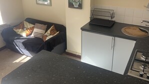 A kitchen with a black countertop, a stove, and a dining area with a couch. - Pretty stone cottage near the village of Pendoylan (Pendoylan)