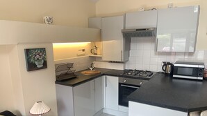 A compact kitchen with a gas stove, microwave, and a kettle. There is a sink with a dish rack, and a small table with a lamp. - Pretty stone cottage near the village of Pendoylan (Pendoylan)
