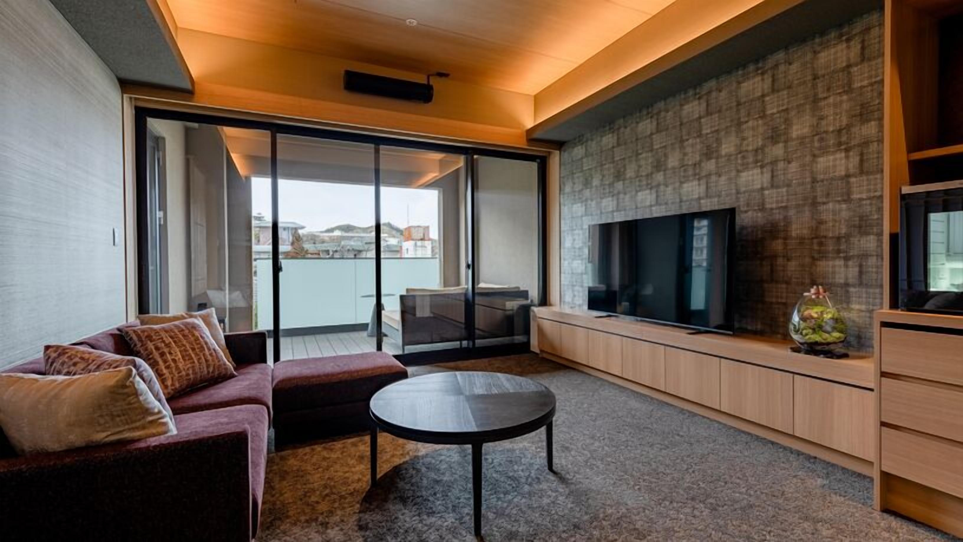 A modern living room with a sofa, a coffee table, a TV, and a sliding glass door leading to a balcony.