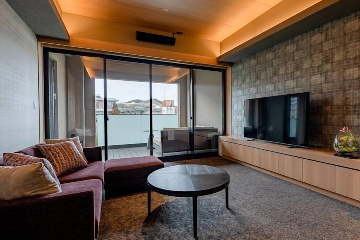 Una sala moderna con sofá, una mesita de centro, televisor y puerta corrediza de vidrio que da a un balcón.