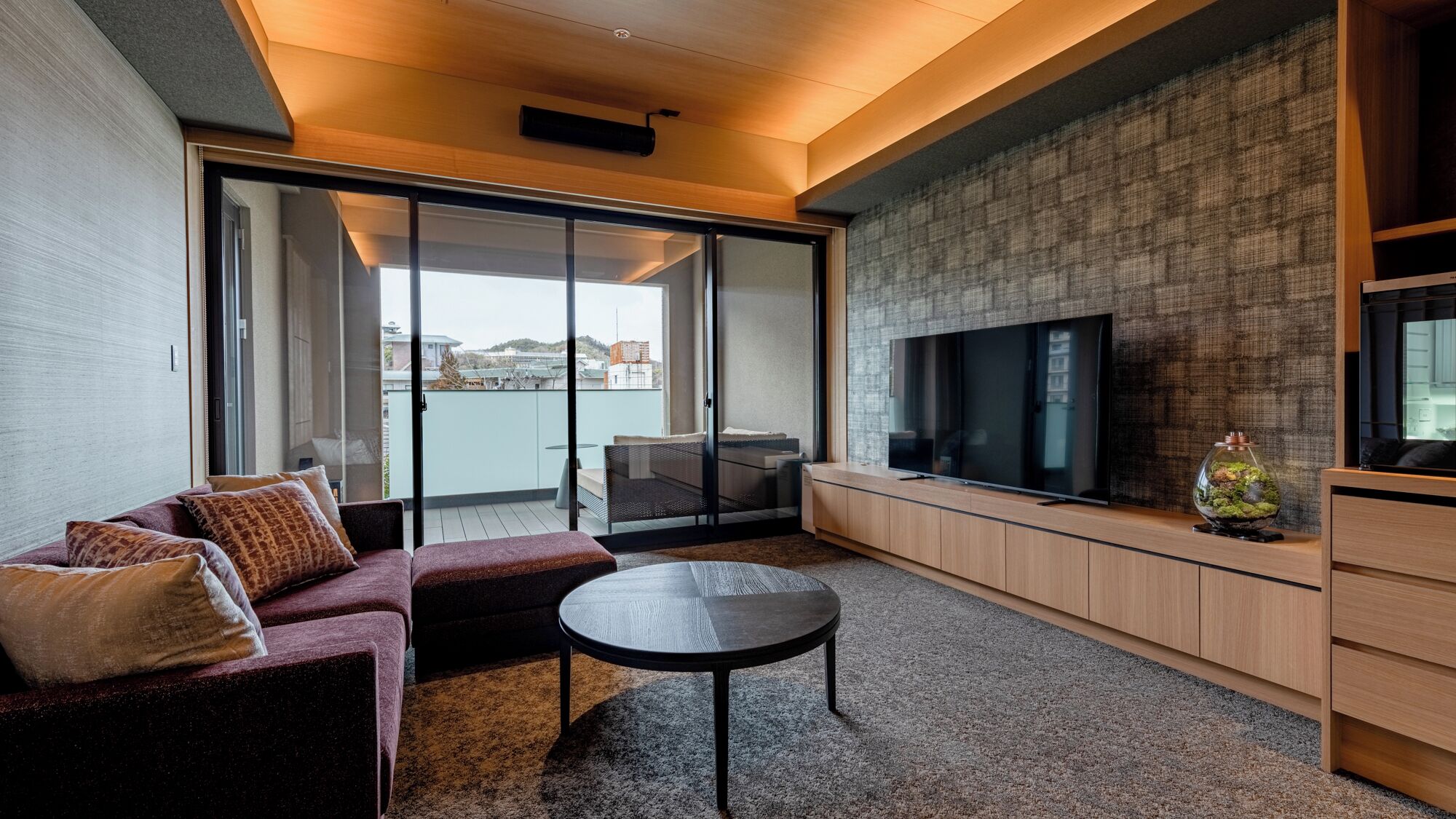 A modern living room with a sofa, a coffee table, a TV, and a sliding glass door leading to a balcony.
